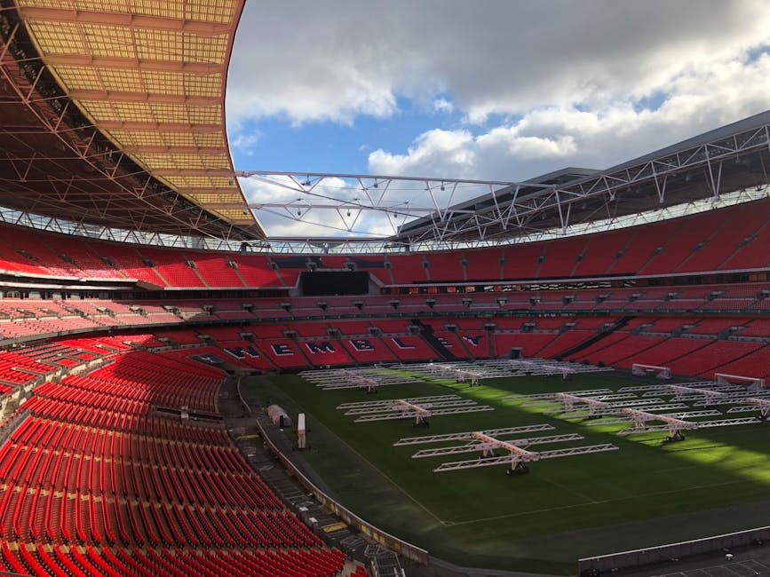 A professional cleaner from Carpet Cleaning NW1 is performing surface deep cleaning inside a dimly lit auditorium, using a vacuum and a hose attachment on a dark carpeted floor. The room features blue